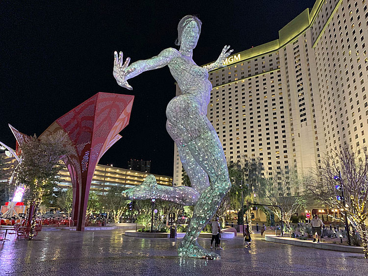 An illuminated dancer sculpture and red shade structure in The Park, with Park MGM behind them at night.