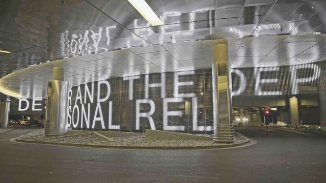 Illuminated text across the ARIA valet wall beneath the reflective entrance canopy.
