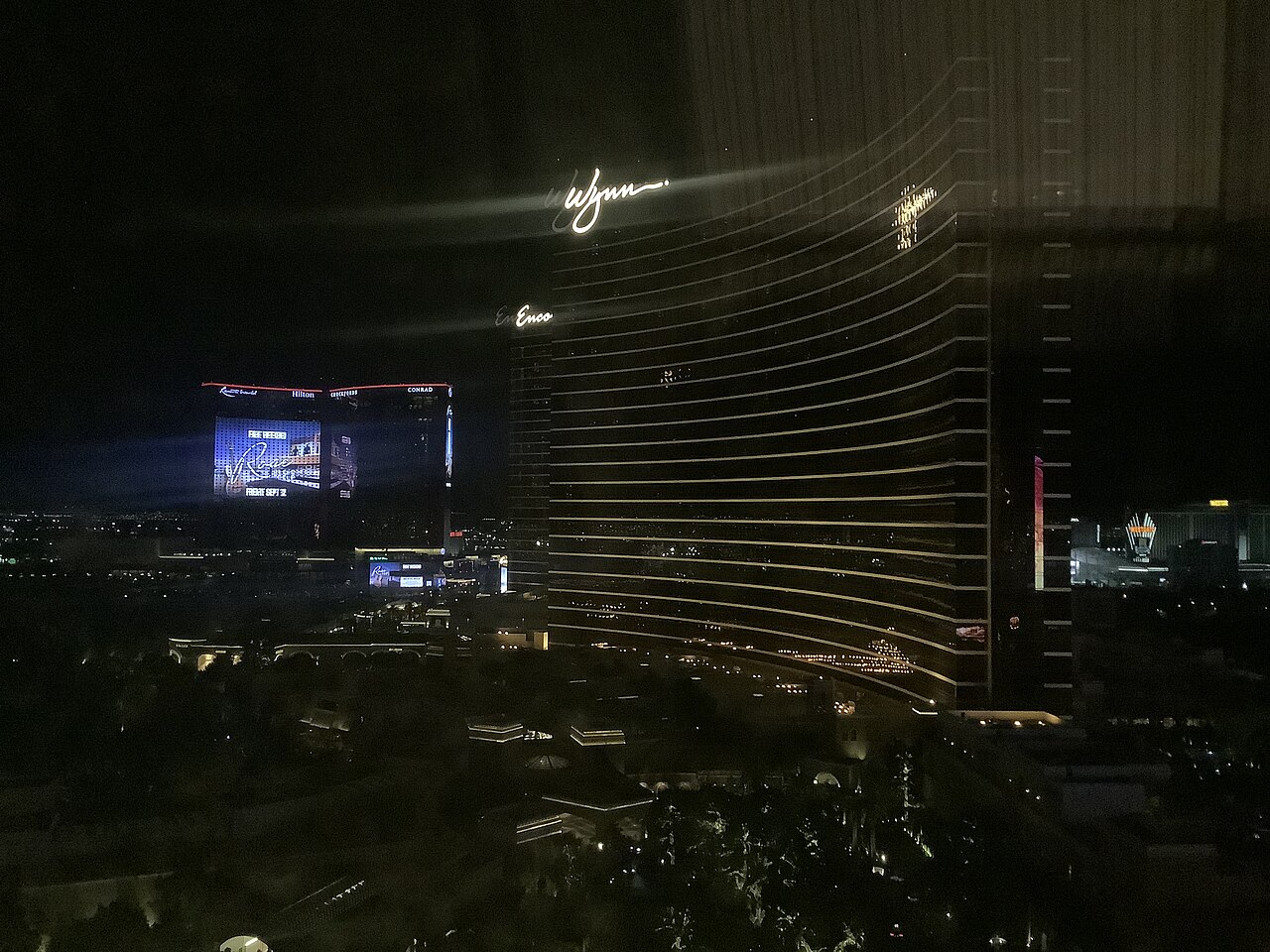 The curved Wynn tower dominates a night view, with Encore behind it and Resorts World at far left.
