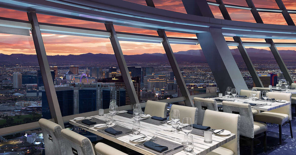 Set dining tables beside the tower’s panoramic windows, with Las Vegas and sunset beyond.
