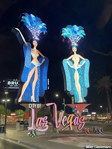 Illuminated showgirl sculptures above the City of Las Vegas sign at night.