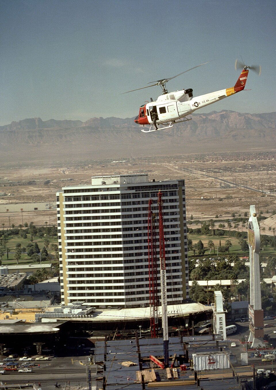 A U.S. Air Force helicopter above a Las Vegas hotel tower, with surrounding streets and mountains.