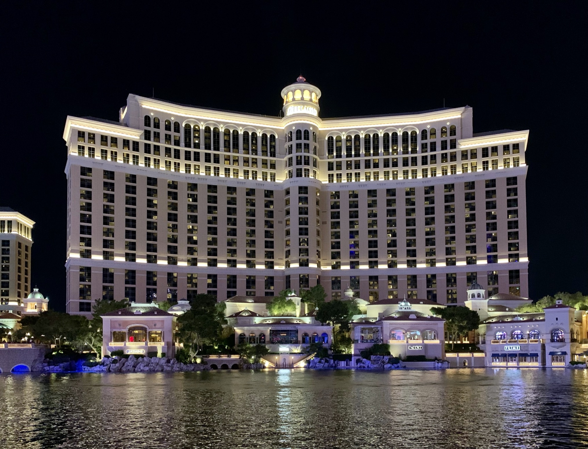 Bellagio’s illuminated hotel tower and lakefront buildings at night.