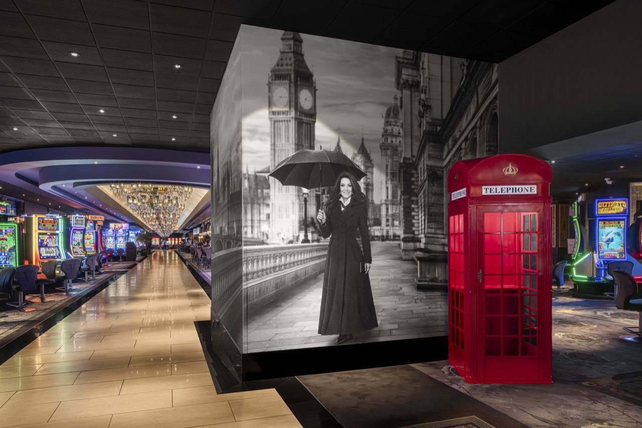 Red telephone box beside a black-and-white London mural featuring Lisa Vanderpump, with casino machines along the corridor.
