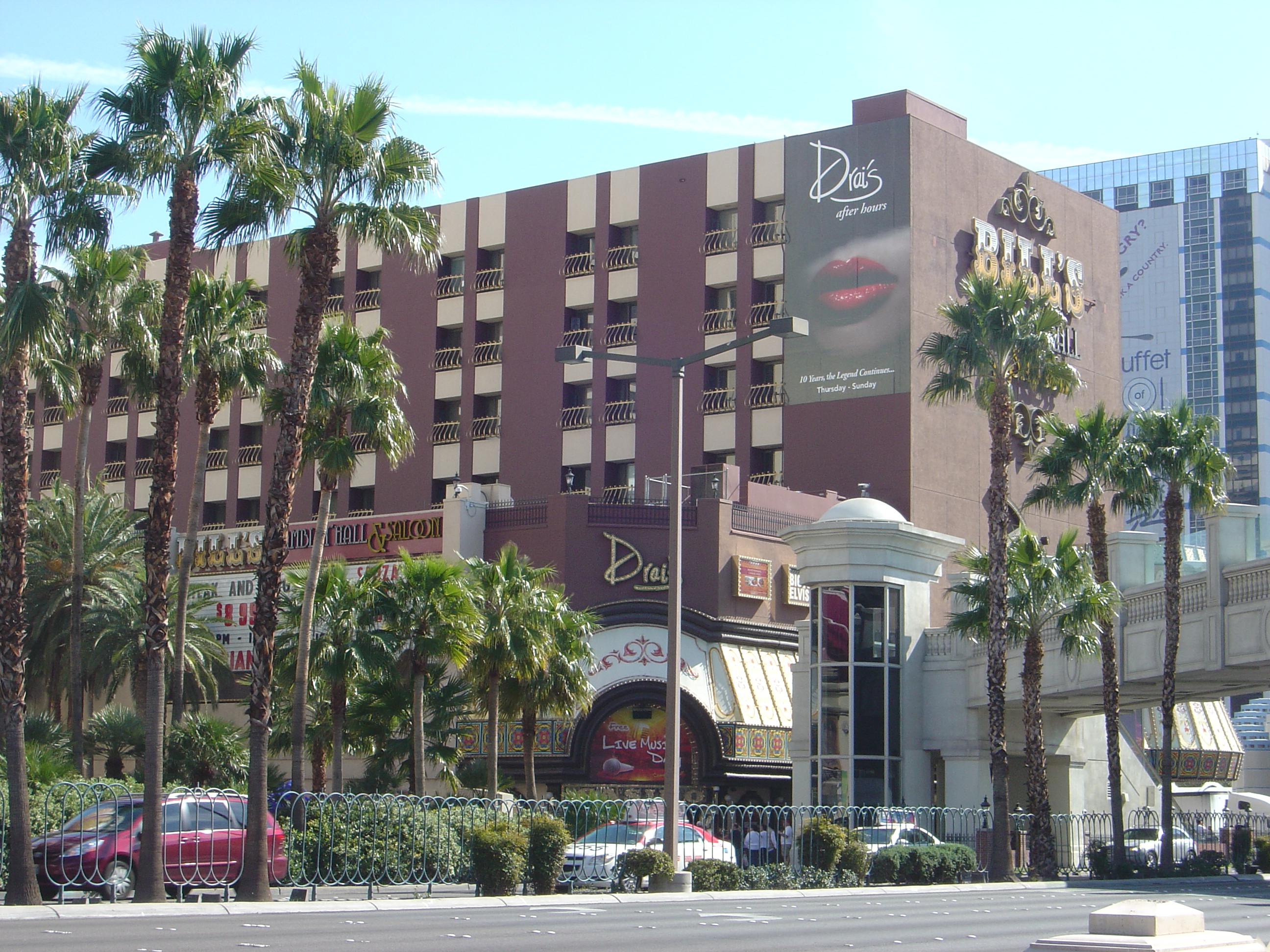 Bill’s brown hotel facade and casino signs behind palms, with the Drai’s sign on the corner.
