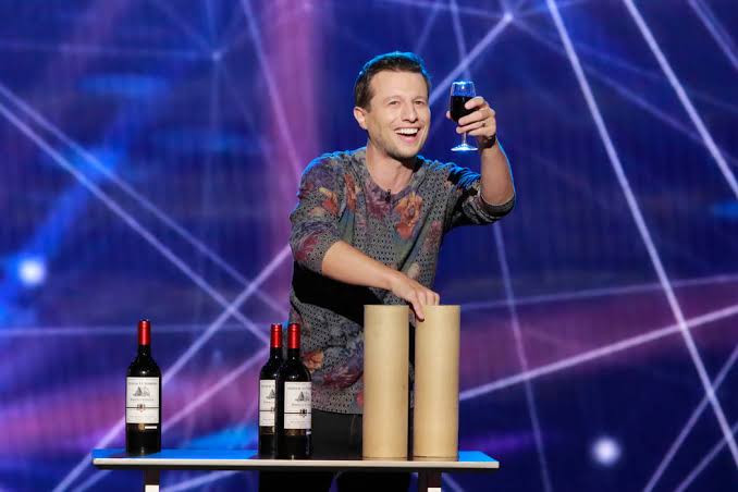 A stage performer with a wine glass, bottles and cylindrical props.