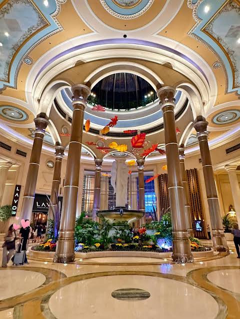 A domed lobby interior with columns, a central fountain and hanging decorations.