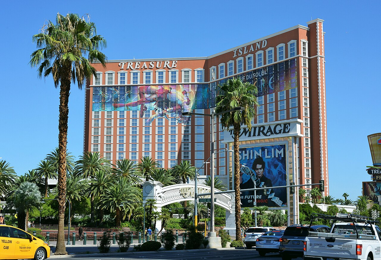 Treasure Island’s peach tower behind palms and a footbridge; the adjacent sign advertises the Mirage and Shin Lim in 2022.