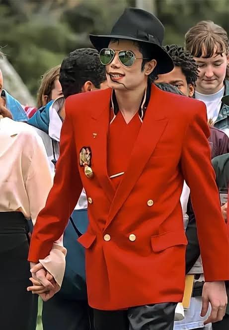 A red double-breasted jacket with gold buttons, black hat and aviator sunglasses.