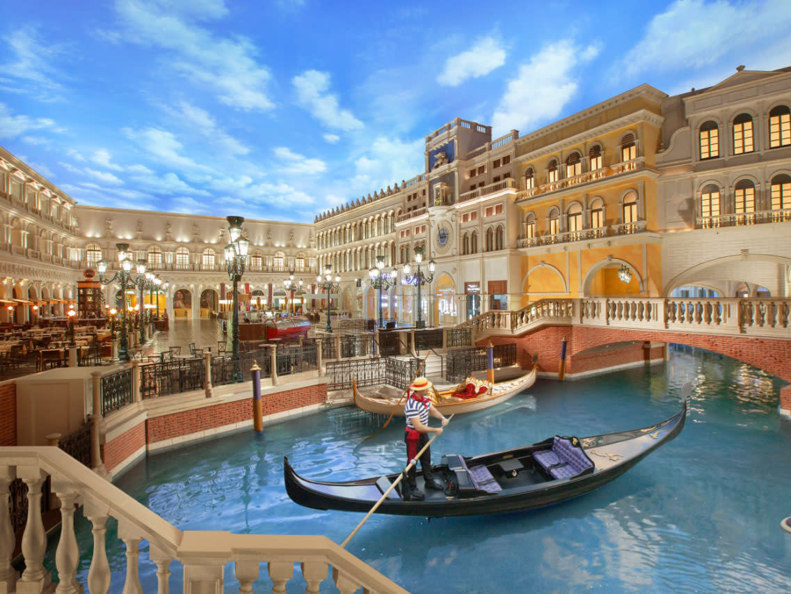 Gondoliers on the indoor canal beneath a painted sky and an arched bridge.