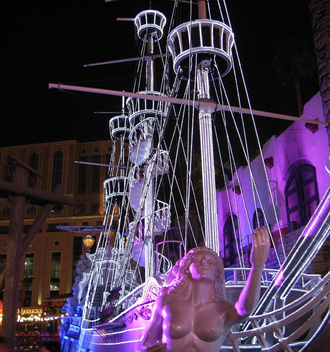 Illuminated ship masts, rigging and a figurehead at Treasure Island at night.