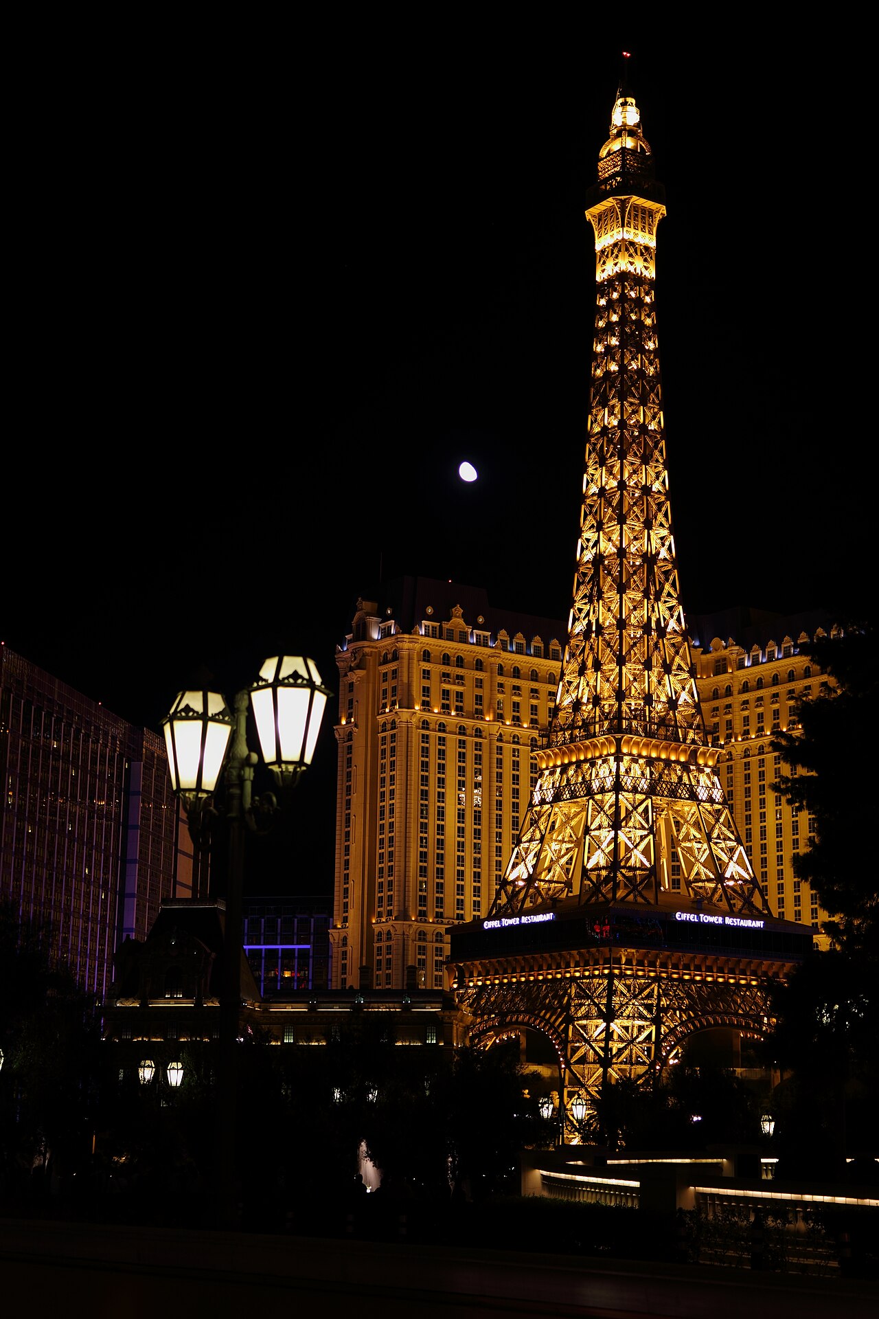 Illuminated Eiffel Tower replica rises beside the Paris hotel under a dark sky.
