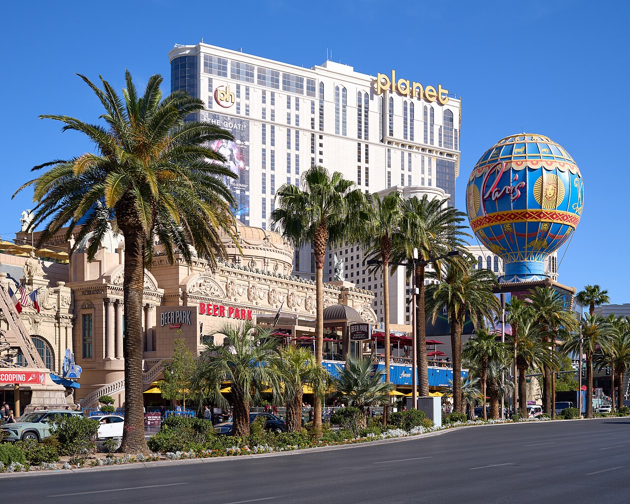 Planet Hollywood’s cream tower and gold planet sign behind palm trees, with the blue Paris balloon beside it.