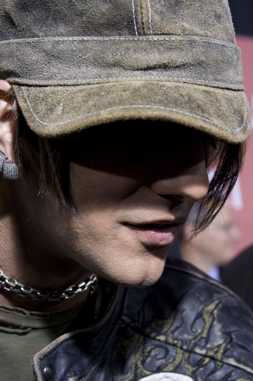 Close portrait of Criss Angel wearing a cap, chain necklace and dark jacket.