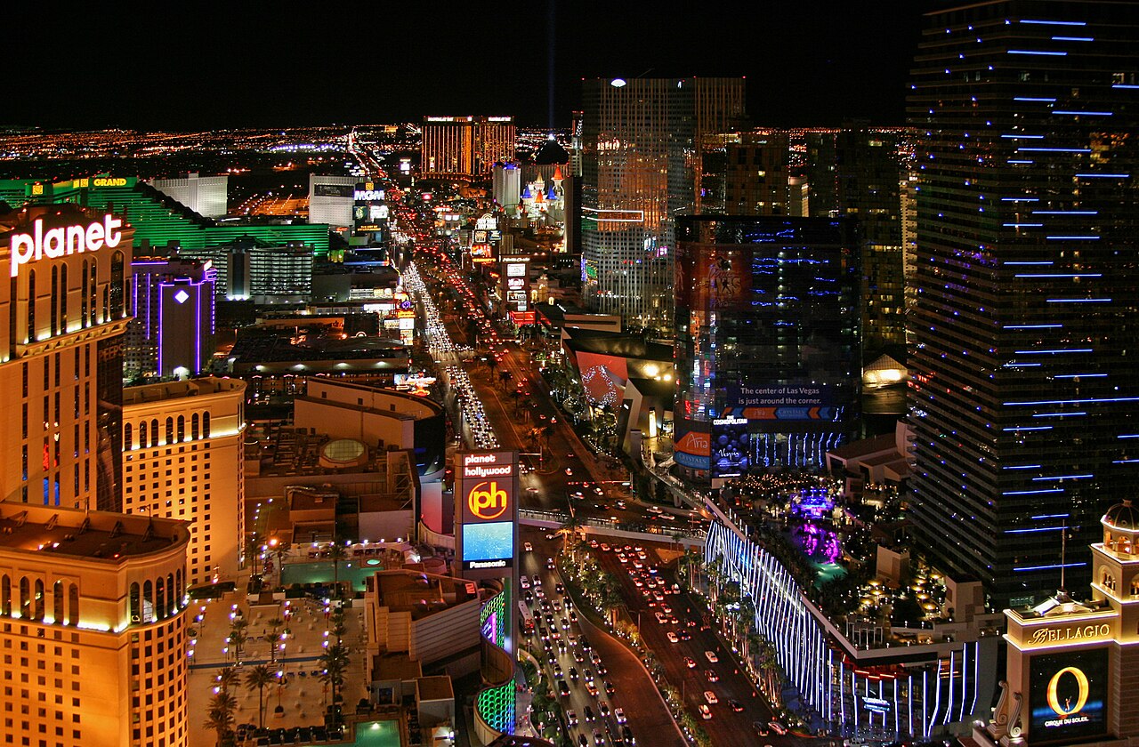 Strip traffic passes between Planet Hollywood and the Cosmopolitan, with MGM Grand in the distance.