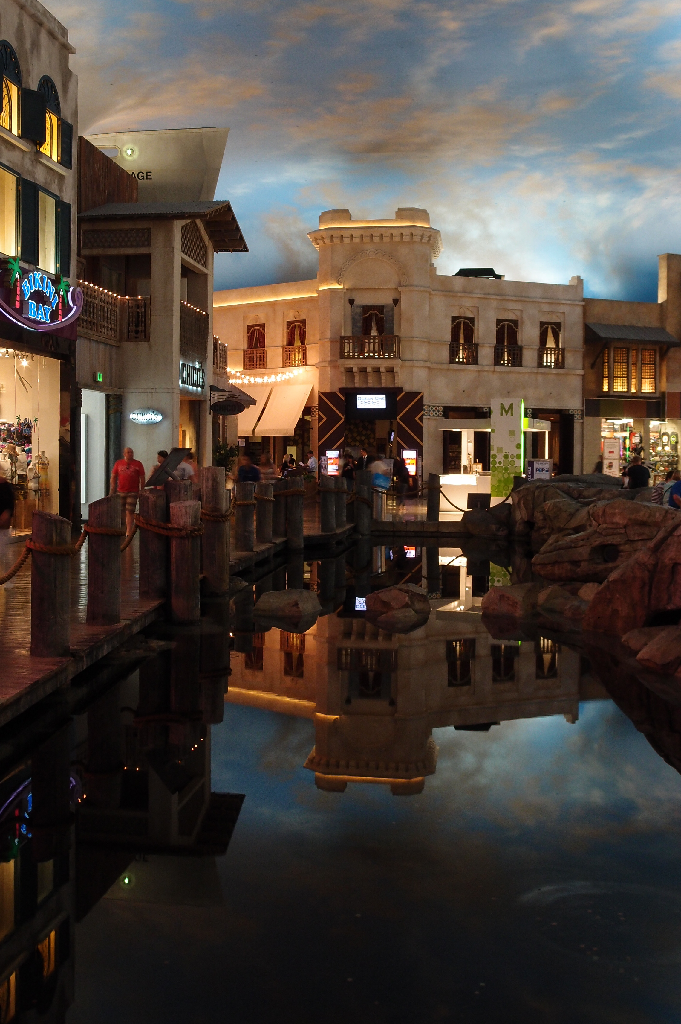 Cream-colored facades and balconies under a blue painted sky, reflected in the indoor water feature.
