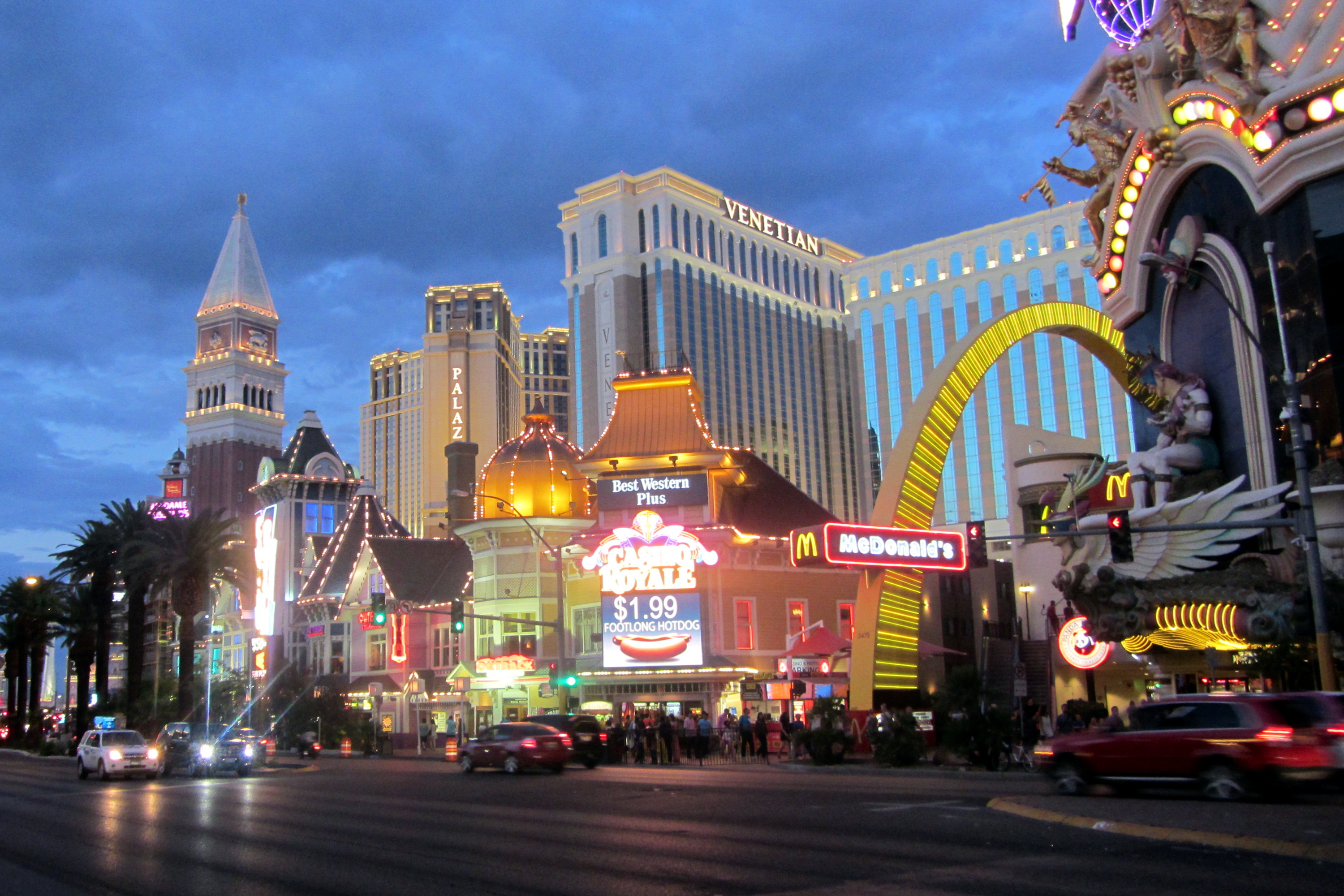 Casino Royale’s illuminated sign advertises a $1.99 foot-long hot dog at dusk, with the Venetian towers behind it.