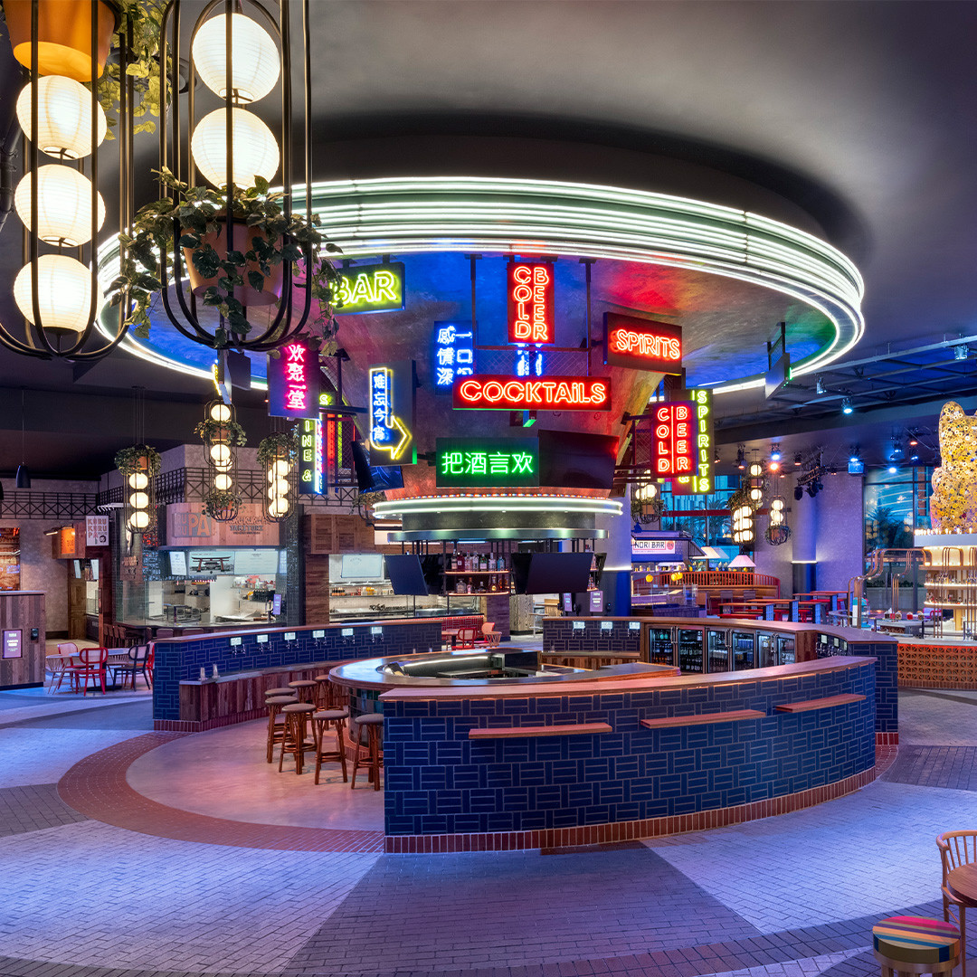 The circular blue-tiled bar and neon signs at Famous Foods Street Eats, with food counters behind it.