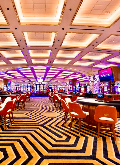 Gaming tables, orange chairs and geometric carpeting on the casino floor.