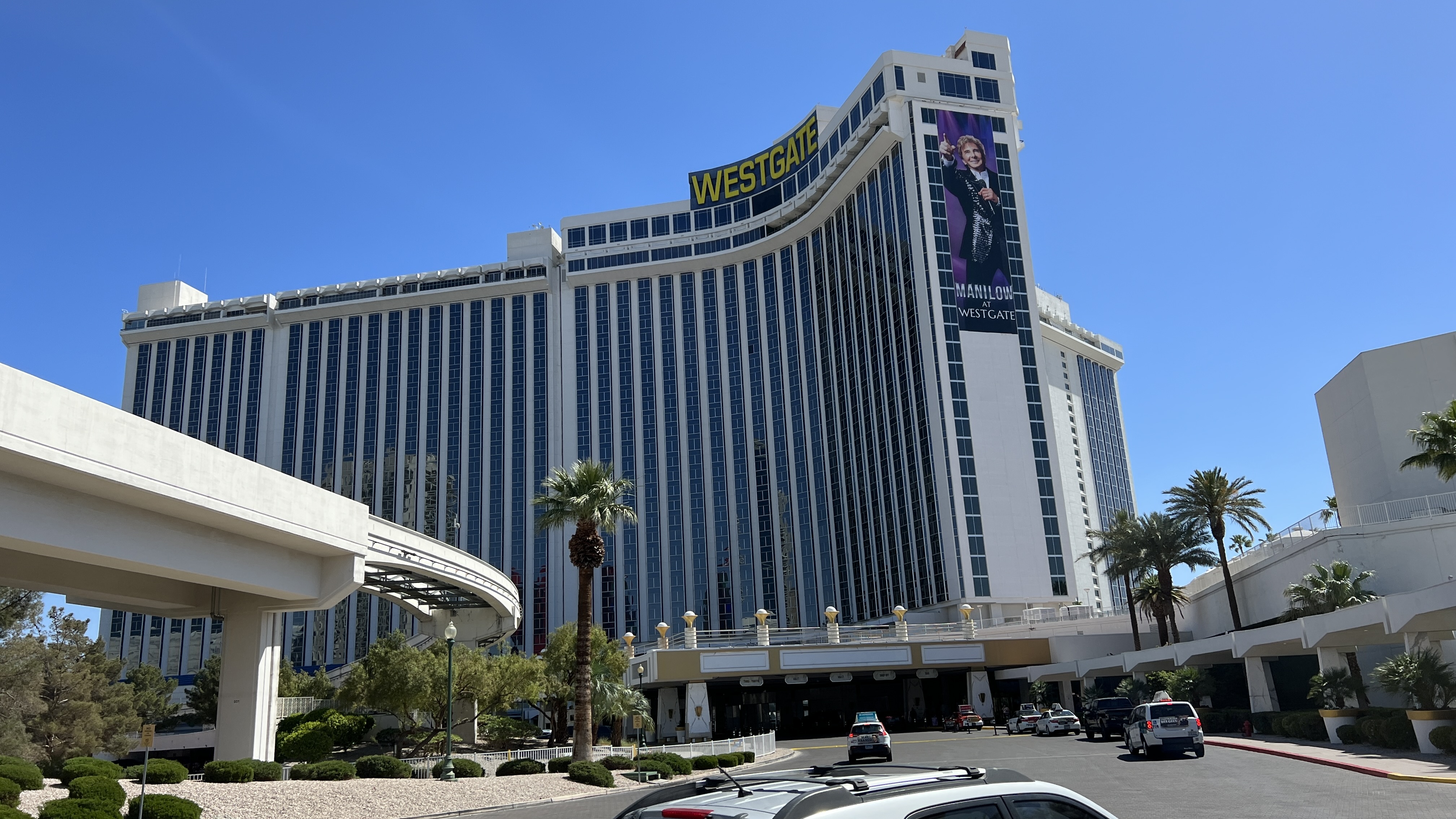 Westgate hotel tower, palms and entrance beneath a blue sky; Westgate sign and Manilow advertisement on the facade.