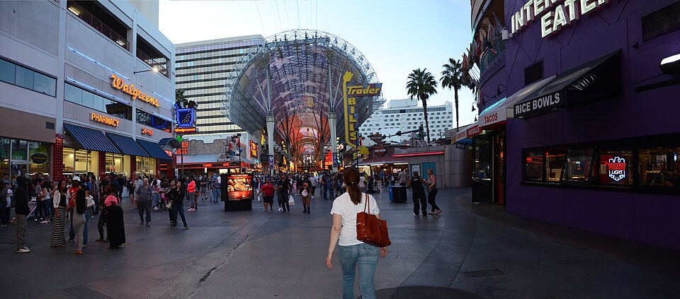 People walking on Fremont Street beneath the canopy, with shop signs and palm trees.