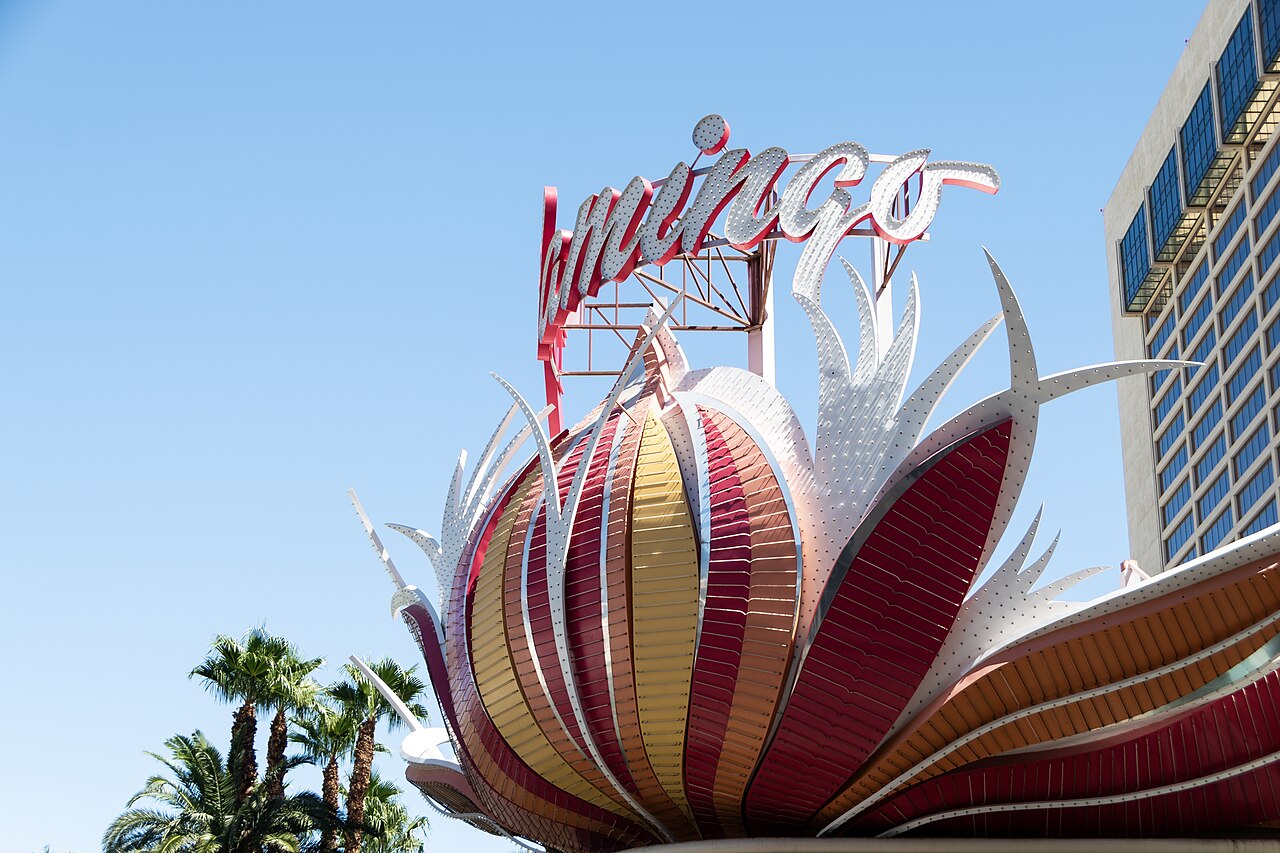 Pink, orange and white feather-shaped signage curls beneath the Flamingo name, with palms and the hotel behind.