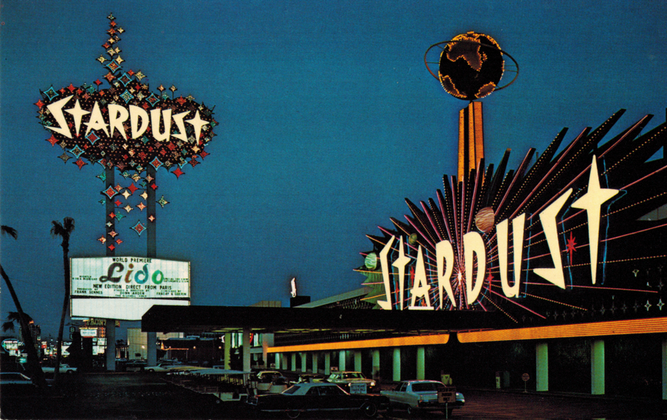 Postcard view of the Stardust Hotel and Casino and its roadside sign.