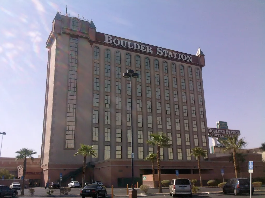 Boulder Station’s tan hotel tower with arched window details and rooftop lettering, seen across a parking area.