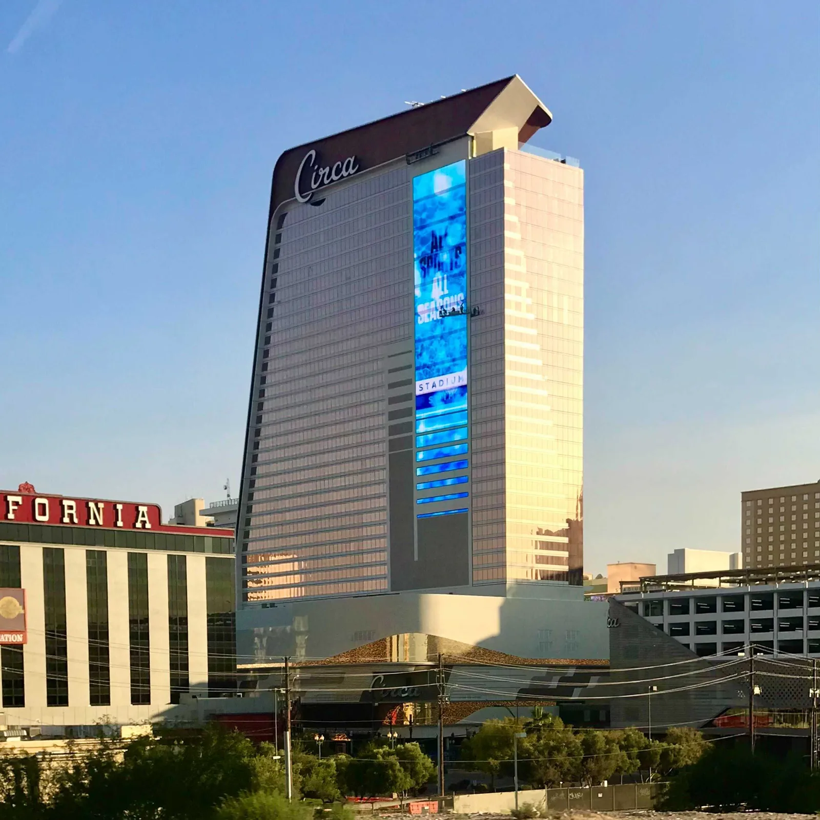 Circa’s tapered hotel tower in late sunlight, with its name and tall digital screen above lower buildings; part of the California hotel appears at left.