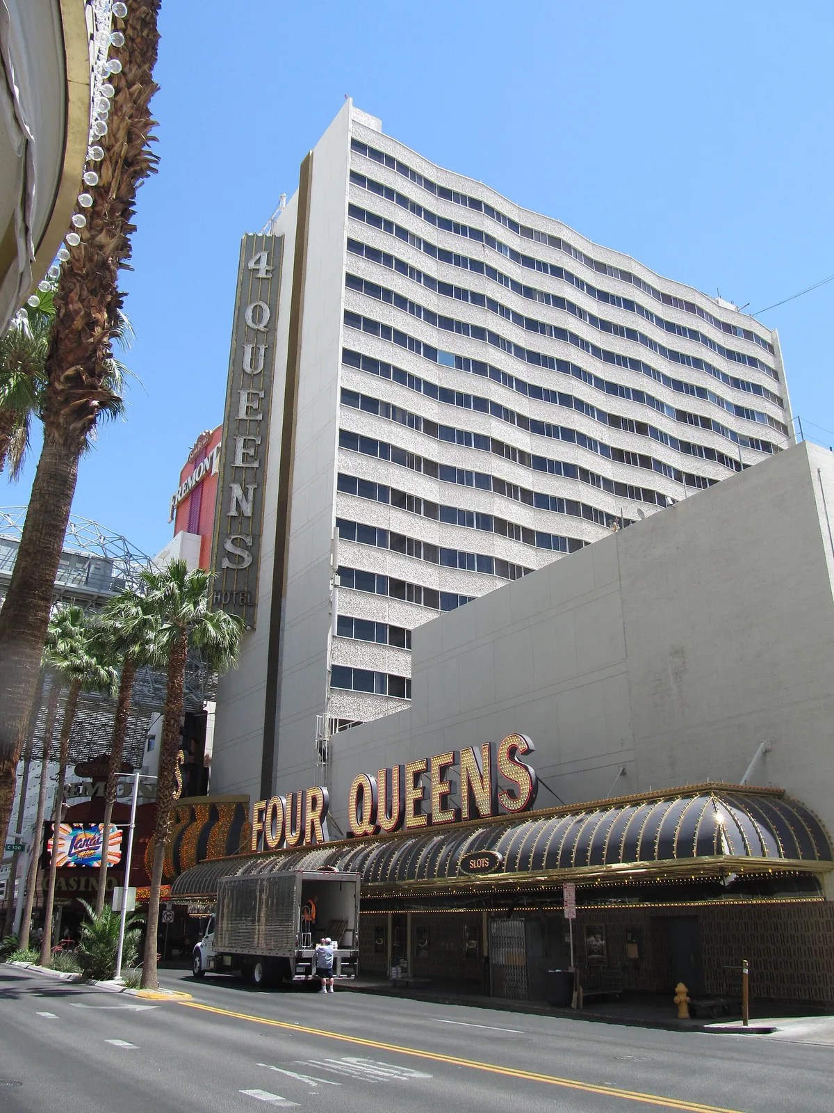 Four Queens’ white hotel tower and vertical sign above its curved casino frontage, with palms along Casino Center Boulevard.