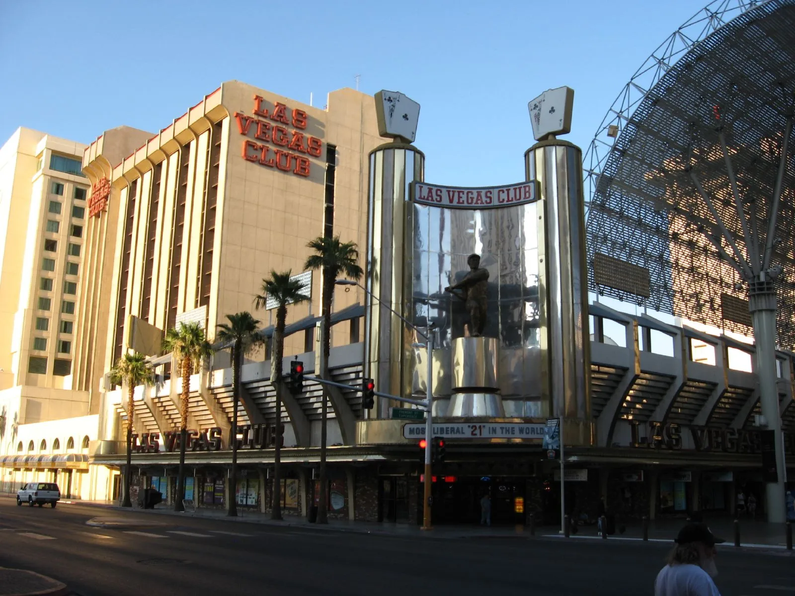 Las Vegas Club’s hotel tower and red lettering beside a mirrored entrance with a ballplayer statue, playing-card signs and the Fremont Street canopy.