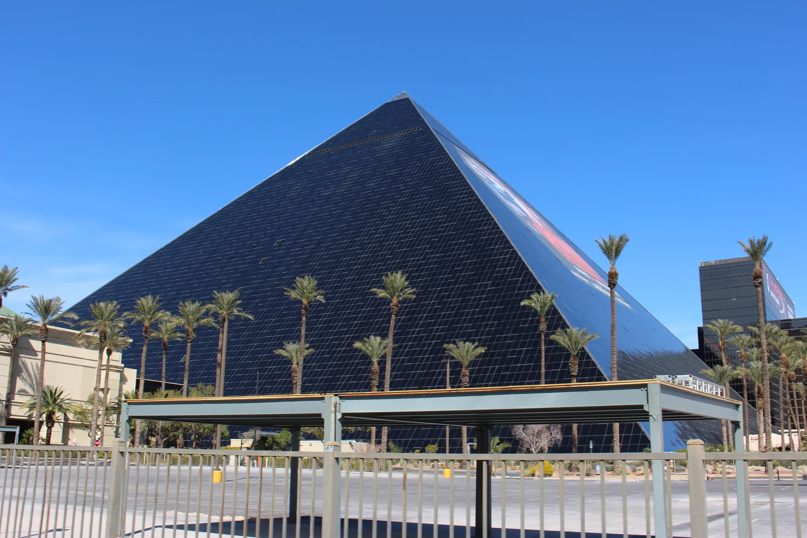 Luxor’s dark glass pyramid and palms under a blue sky in 2020, behind the foreground tram structure; a later hotel tower stands at right.