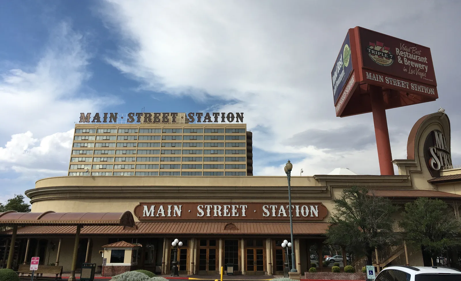 Main Street Station’s low casino frontage, hotel tower and tall Triple 7 restaurant and brewery sign beneath a cloudy sky.
