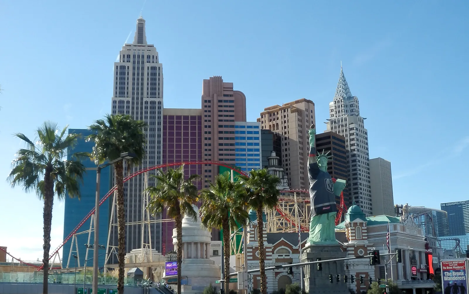 New York-New York’s themed hotel towers and red roller coaster behind its Statue of Liberty in a dark hockey jersey, with palms in the foreground.