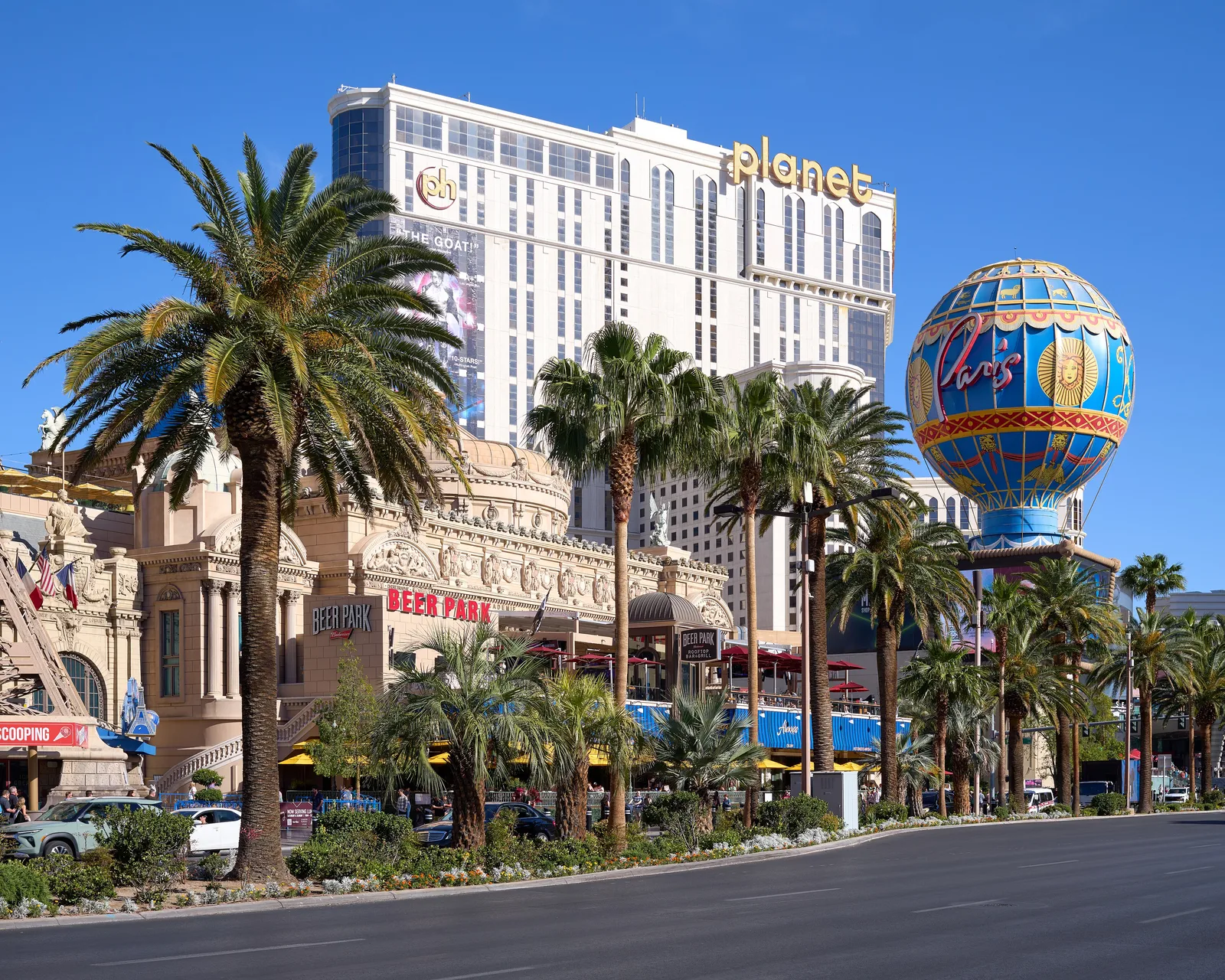 Paris Las Vegas’s ornate frontage, Beer Park terrace and blue balloon sign in 2026, with palms and the separate Planet Hollywood tower in the background.