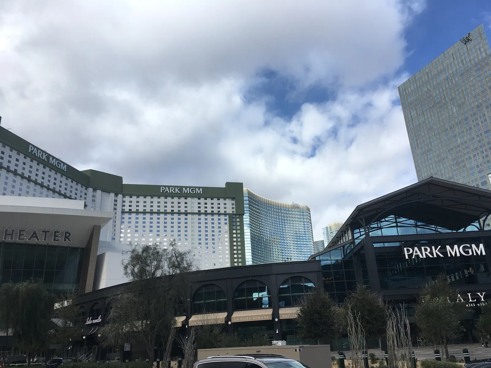 Park MGM’s white tower and green signs behind its lower frontage in 2019; separate ARIA and Waldorf Astoria buildings rise behind it.