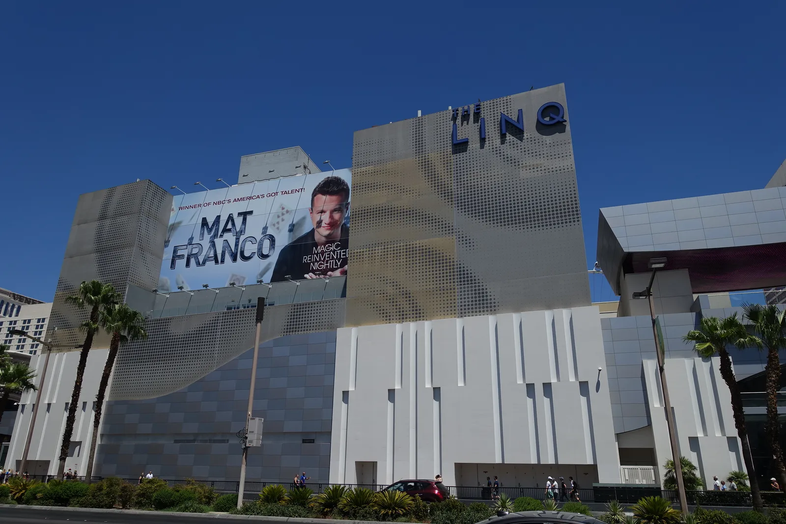 The LINQ name on a perforated geometric facade, beside a large Mat Franco advertisement, palms and the Strip in July 2017.