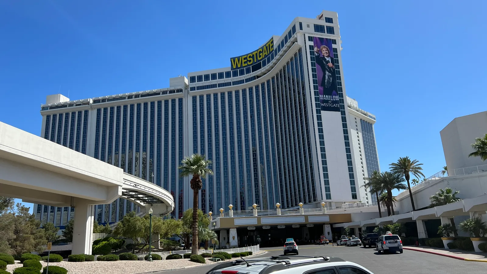 Westgate’s curved hotel tower above its entrance and palms, with a large Barry Manilow banner and an elevated monorail at left in 2022.